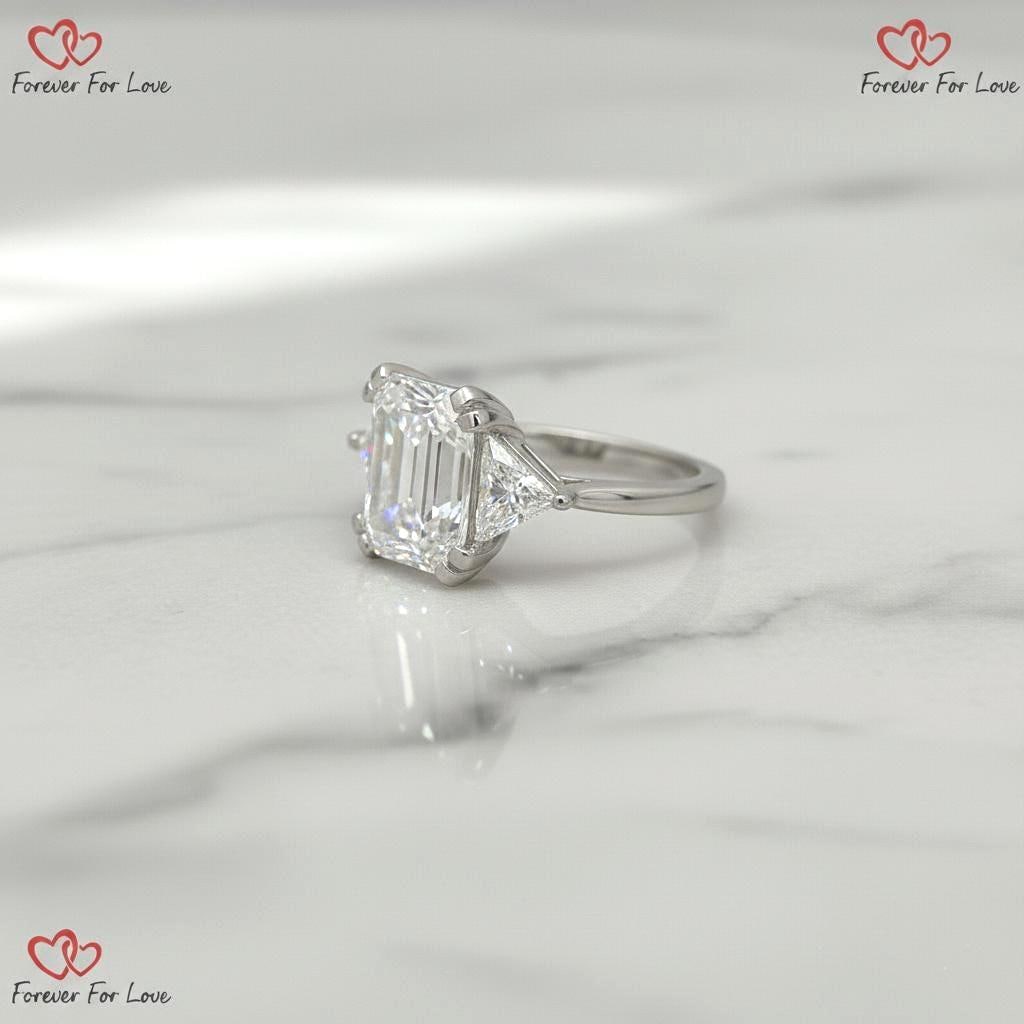 Bague de fiançailles trilogie avec diamants de synthèse taille émeraude 6 carats couleur E pureté VVS2 certifiés IGI et taille trillion sur les côtés, or blanc 18 carats Emerald cut Moissanite engagement ring in Gold or Platinum — custom handcrafted by Forever For Love